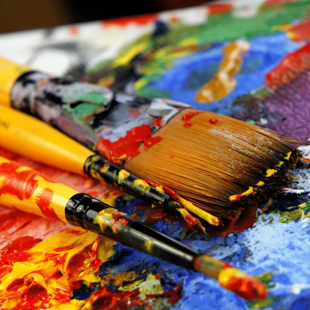 Close-up of colorful paintbrushes on a palette with various shades of paint, representing creativity and art therapy.